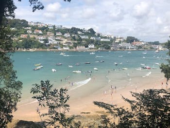 A stunning, sandy beach in Salcombe featuring people having fun on the sand, in the sea or in a wide variety of boats