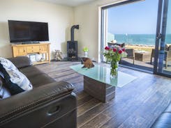 Living area with log burner, widescreen TV and balcony access overlooking the sea