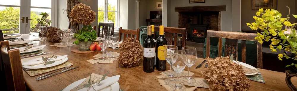 Dining table set ready to welcome guests with wine, natures offerings of herbs, fruit and flowers decorate the table.
