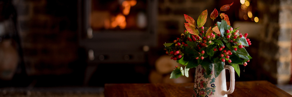 Cosy fireside scene. Seasonal flowers arranged in jug.