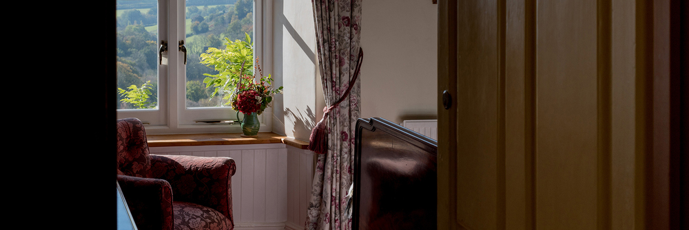 A peek through the door into a a bedroom and view through the window beyond