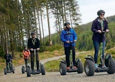 A groupd of 5 people are smiling as they travel by Segway through the Forest of Dean