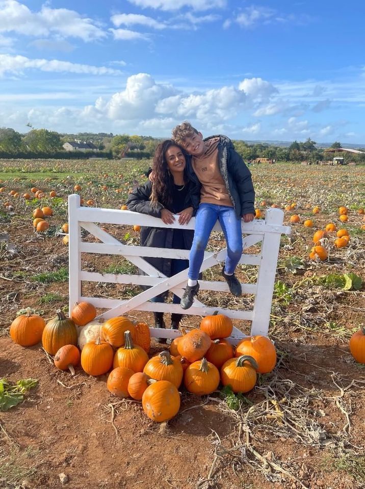 Women and boy smiling in front of a pumpkin patch
